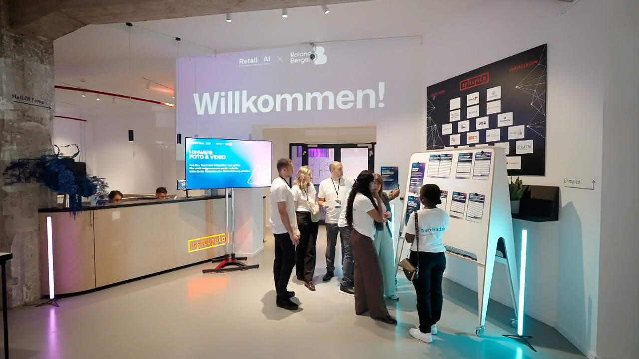 Eingangsbereich des Retail-KI-Festivals mit Angestellten vor Programmtafeln